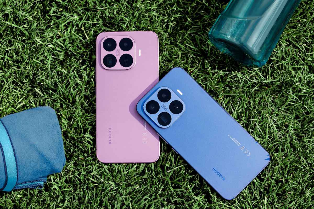 Du Xiaomi išmanieji telefonai guli ant žalios vejos šalia mėlynos rankšluosčio dalies ir mėlynos stiklinės butelio